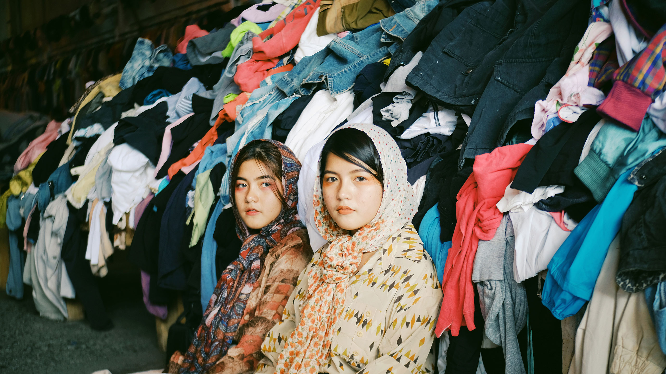 2 girls sitting in front of a pile of clothes