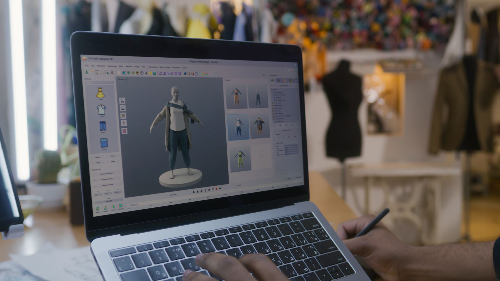 Designer working on a laptop using 3D software for digital fashion design in a studio with a dress form in the background.