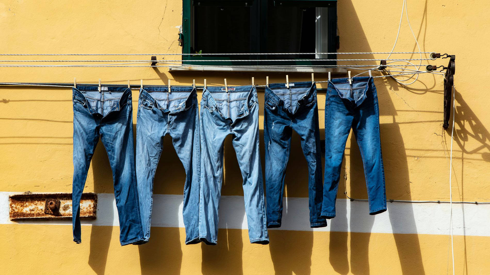 Jeans hanging to dry on clothesline against yellow wall in the sun