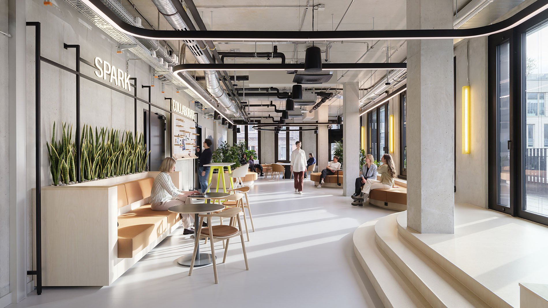 Bright communal area with industrial loft character, plants, and modern seating