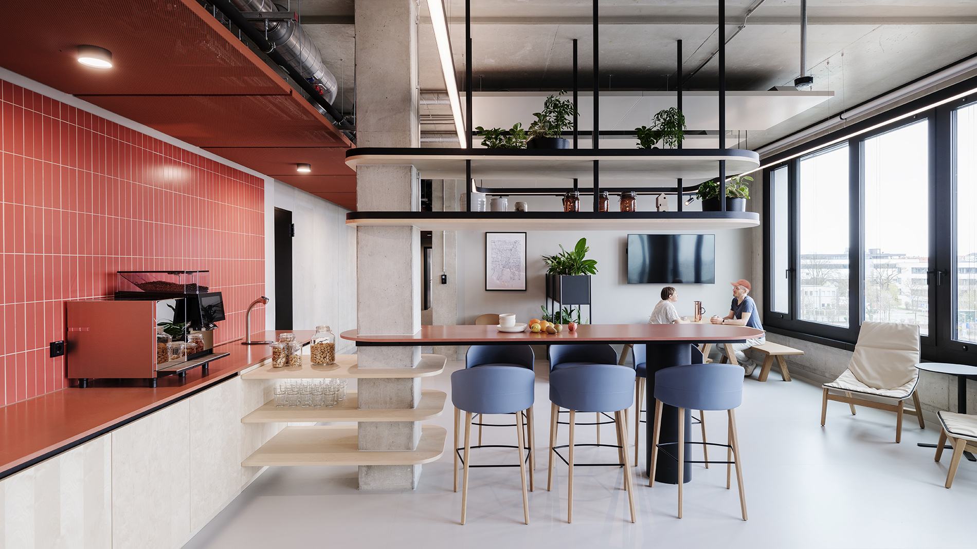 Open office kitchen with red tiles, modern seating, and greenery