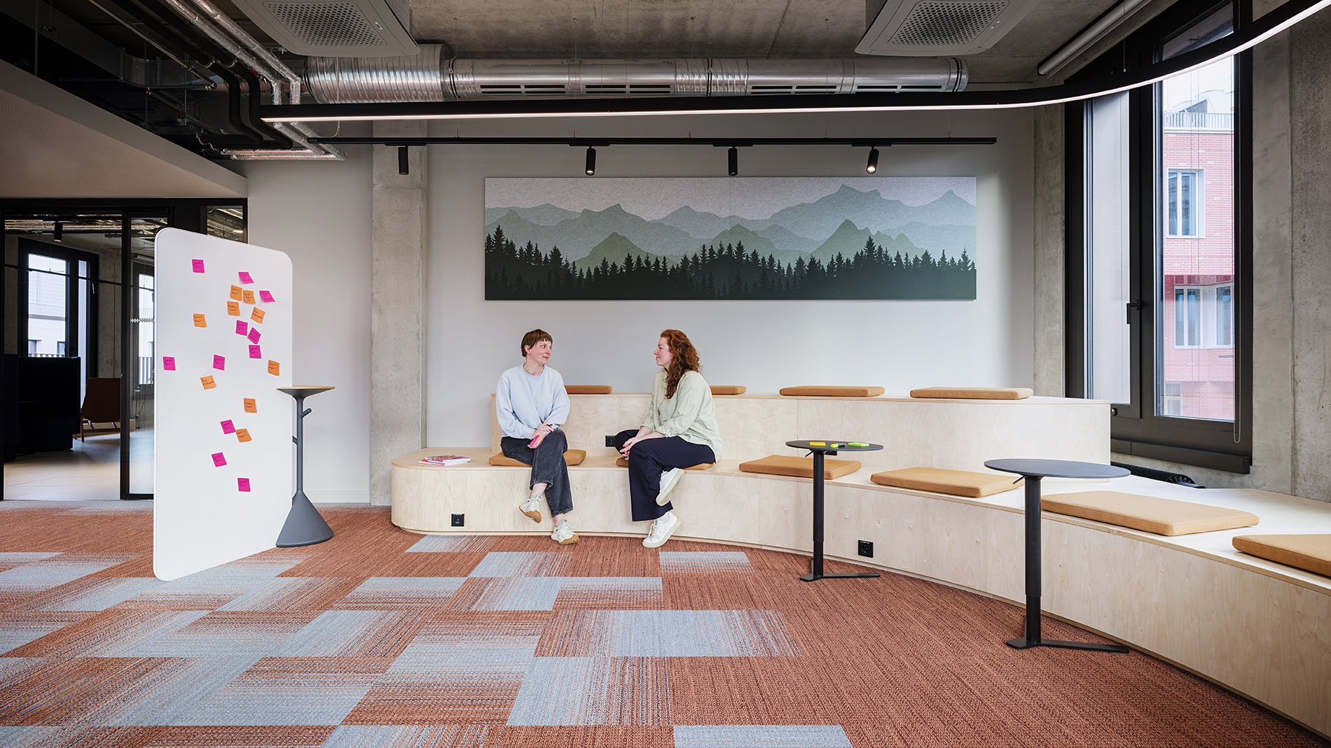 Creative meeting space with semi-circular wooden seating and a mountain landscape wall