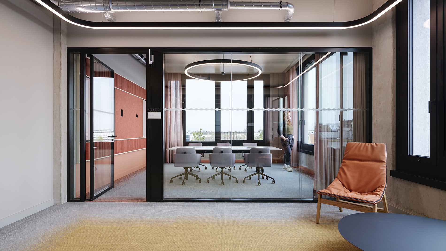View into a modern conference room with glass walls, ergonomic chairs, and a warm colour palette in yellow and pink tones.
