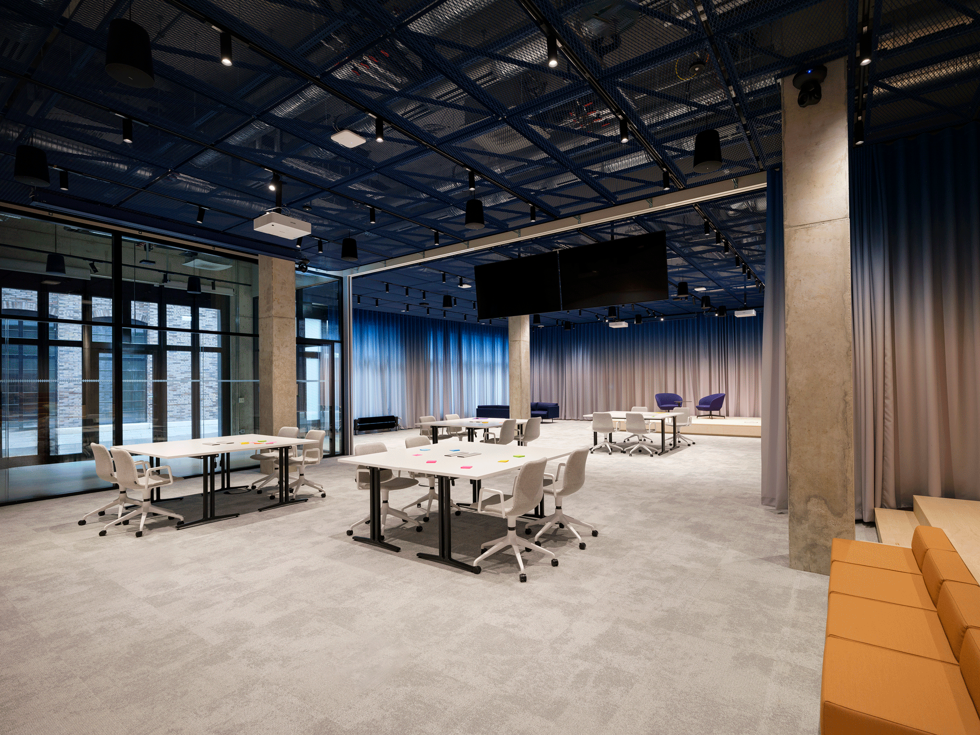 Open workspace with flexible desks, grey carpeting, and blue ceiling design, ideal for collaborative work in a modern office.