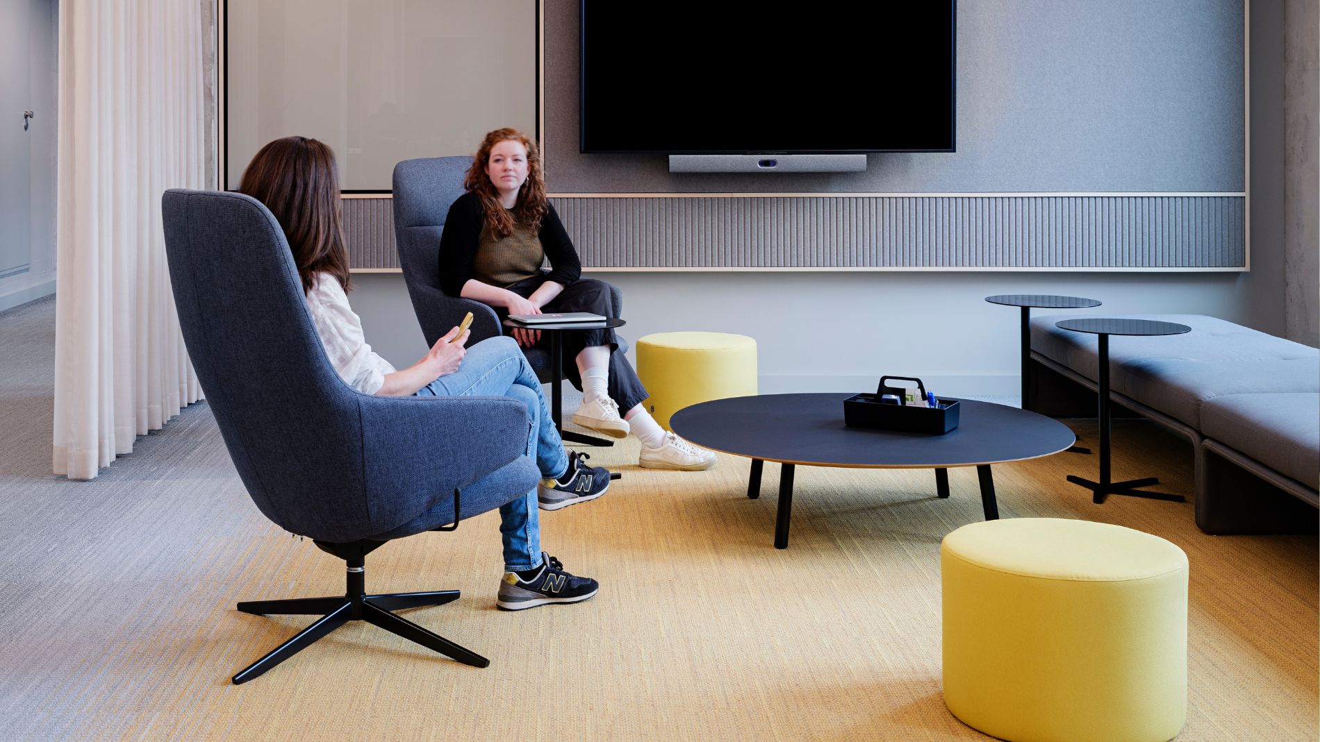 Meeting room with grey chairs, yellow accents, and a screen