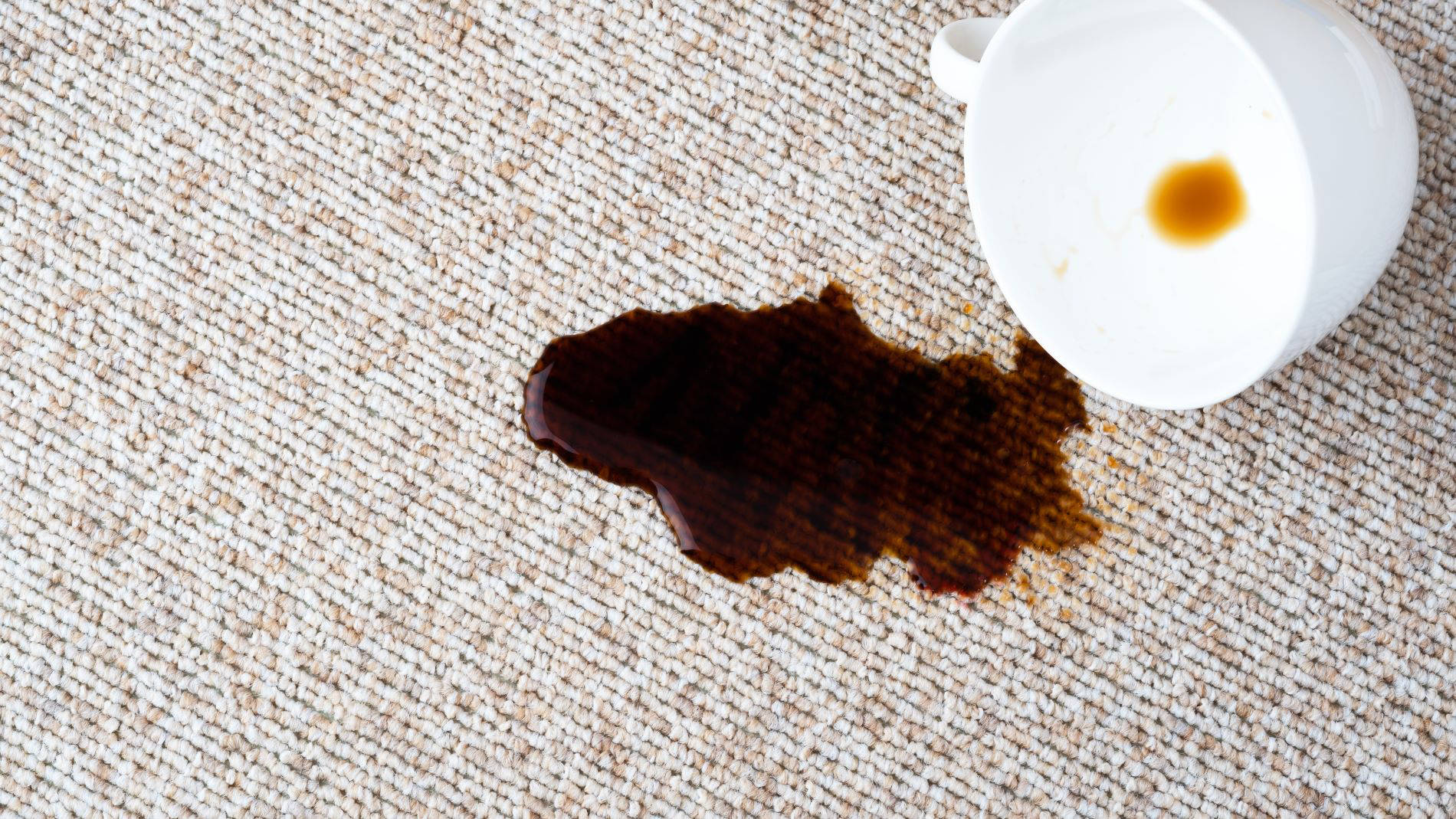Umgefallene Tasse und Kaffedfleck auf einem Teppichboden