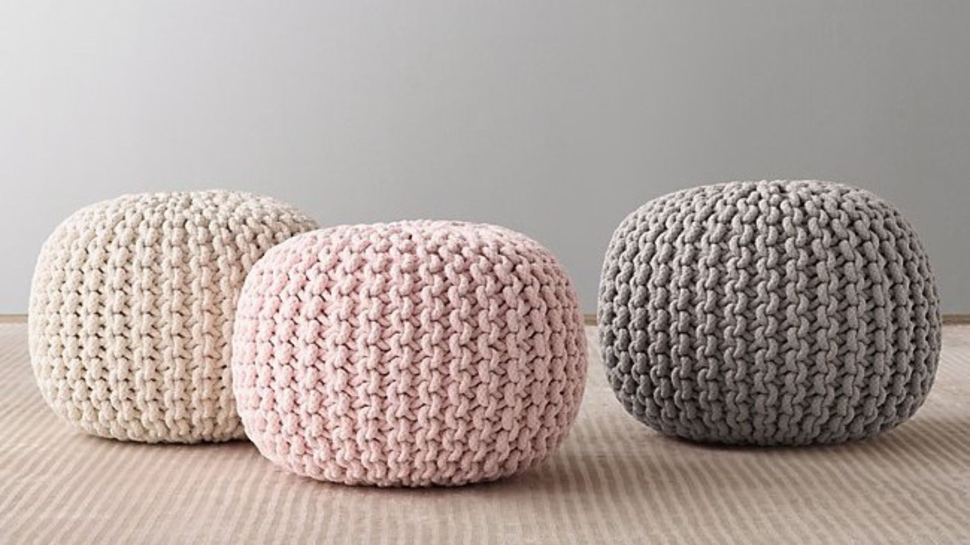 Three knitted poufs in pastel colours on a light carpet