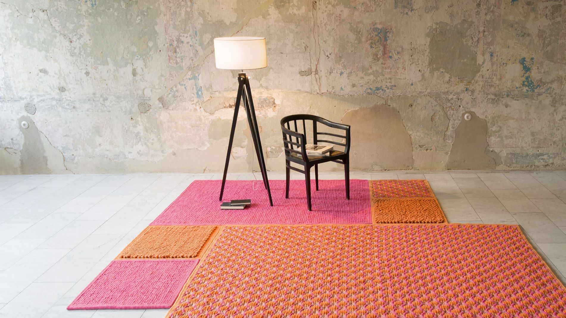 Modern room with colourful rugs, chair and floor lamp against a textured wall