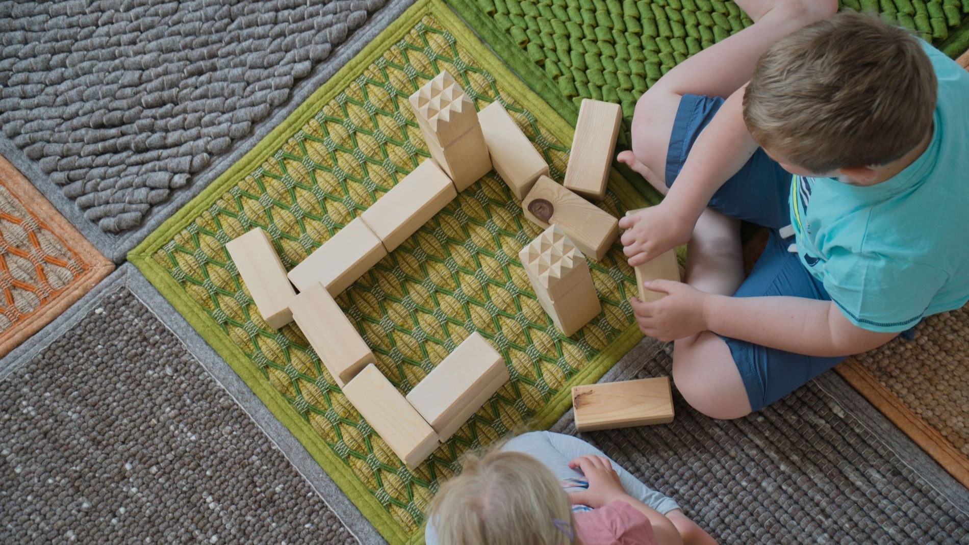 Children playing with wooden blocks on textured rugs in natural colours