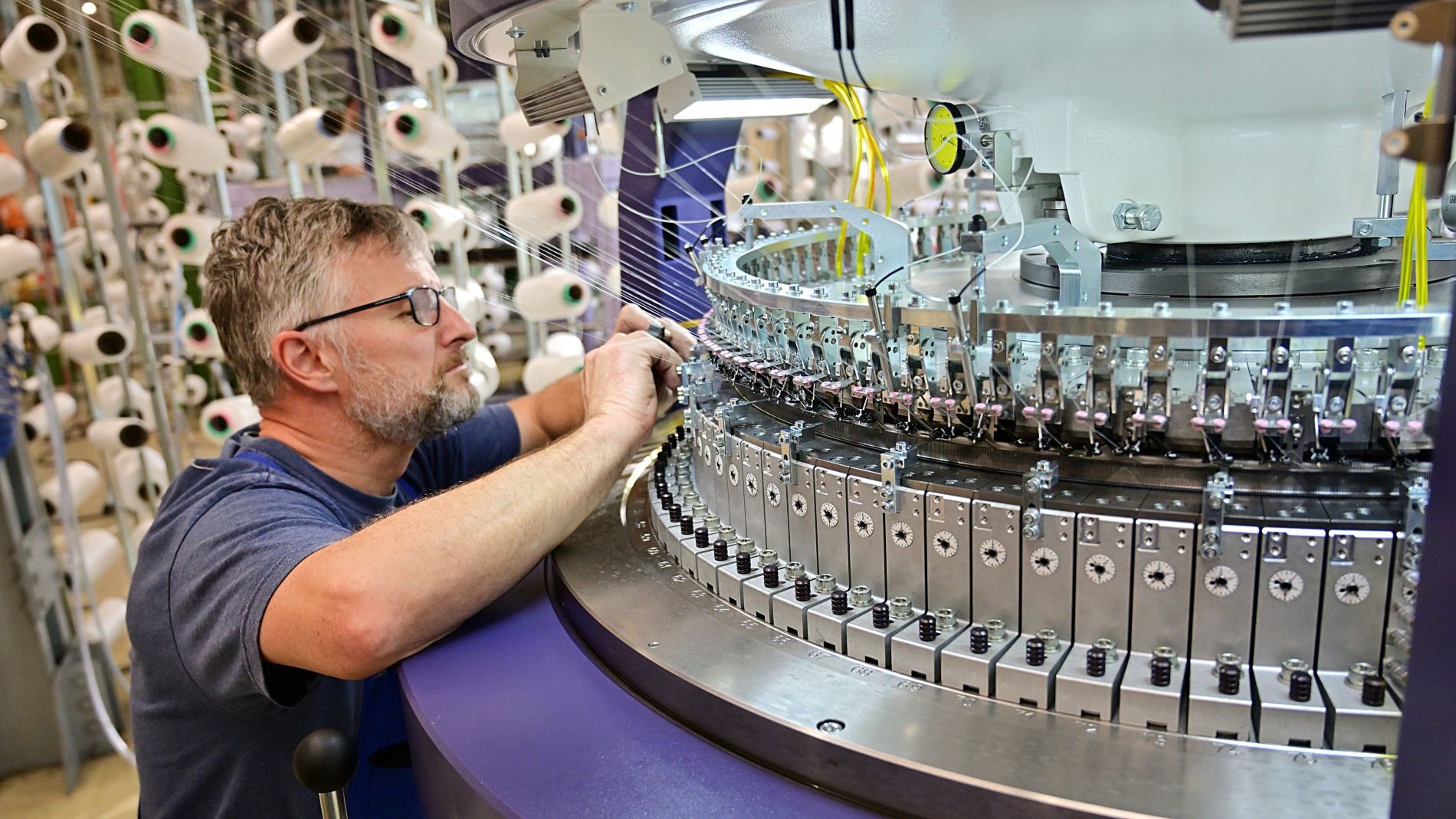 Technician working on an industrial circular knitting machine in textile production