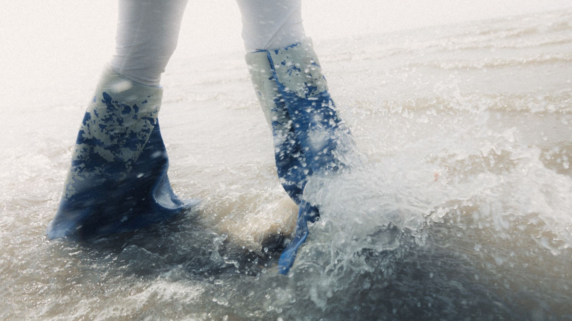 Blue boots in the sea water on the beach