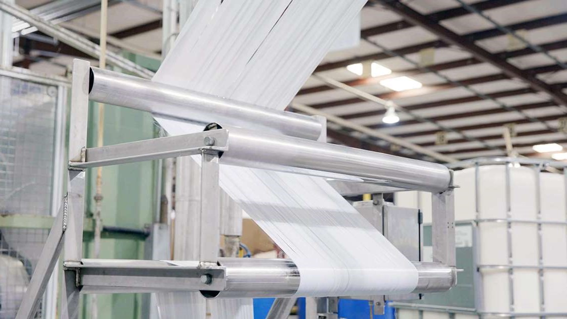 Textile sheet running through industrial guide rollers.